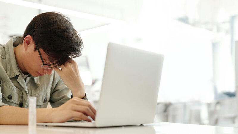 Man sitting in front of laptop experiencing a migraine